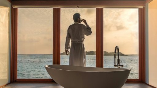 man standing in bathroom with bathtub next to body of water