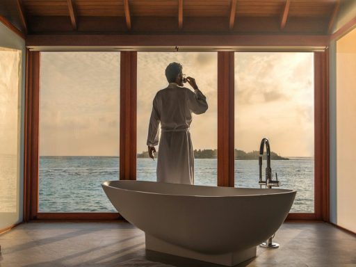 man standing in bathroom with bathtub next to body of water