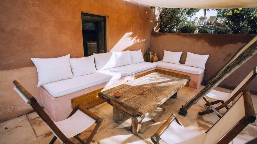 Inviting outdoor patio with rustic wooden furniture and white cushions, perfect for relaxation.