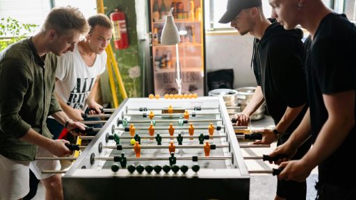 Four young men intensely playing foosball in a lively indoor space.