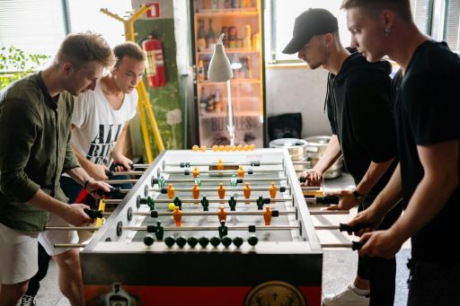Four young men intensely playing foosball in a lively indoor space.