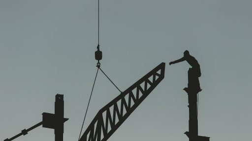 silhouette of man standing on top of tower crane