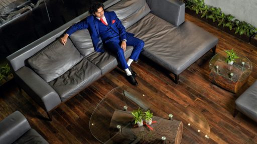 man in blue jacket and blue denim jeans sitting on gray couch