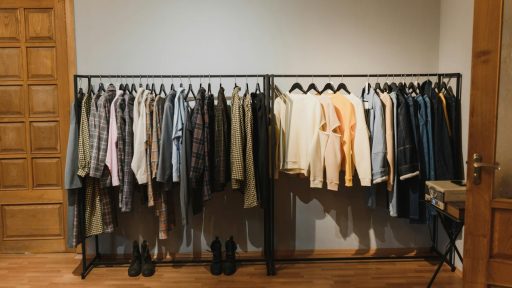 A neatly arranged indoor clothing rack with various garments on hangers in a wooden-floored room.