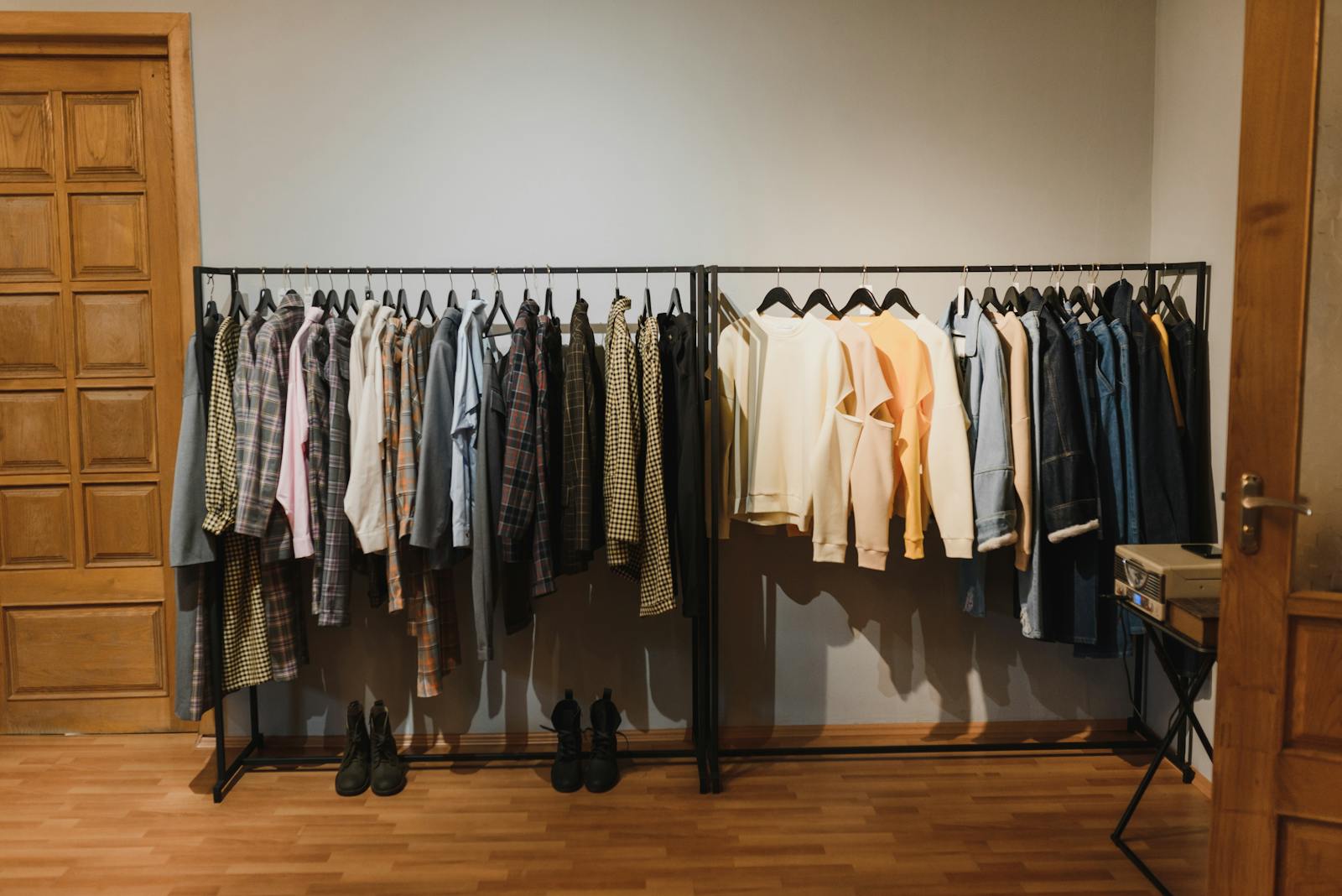 A neatly arranged indoor clothing rack with various garments on hangers in a wooden-floored room.