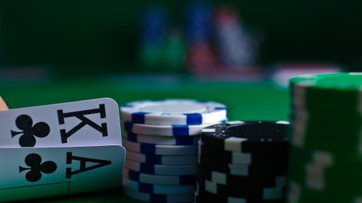 A hand holding playing cards beside stacks of poker chips on a green table
