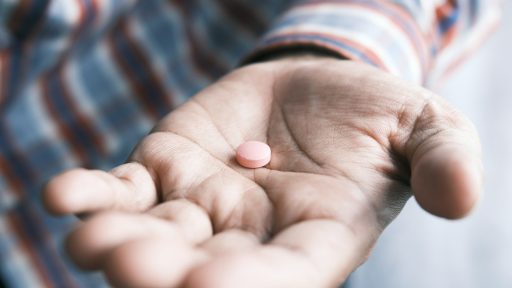 person holding pink round medication pill