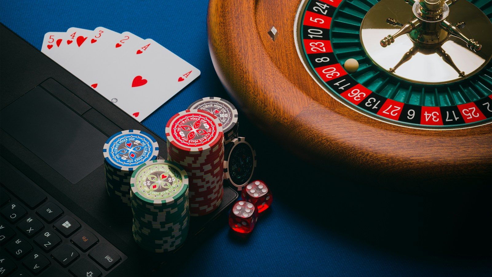 A roulette wheel, poker chips, playing cards, and dice on a laptop keyboard